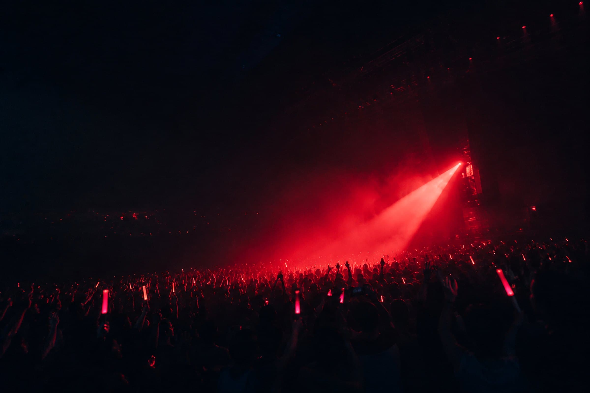 Kerumunan penonton konser mengangkat tangan menghadap panggung bermandikan cahaya merah